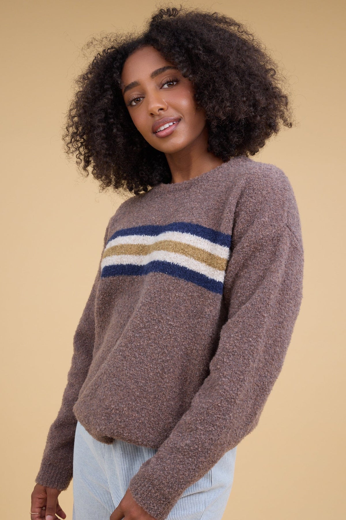 A young woman wearing a  modest brown sweater with a wide, multicolor chest around the chest with long sleeves.