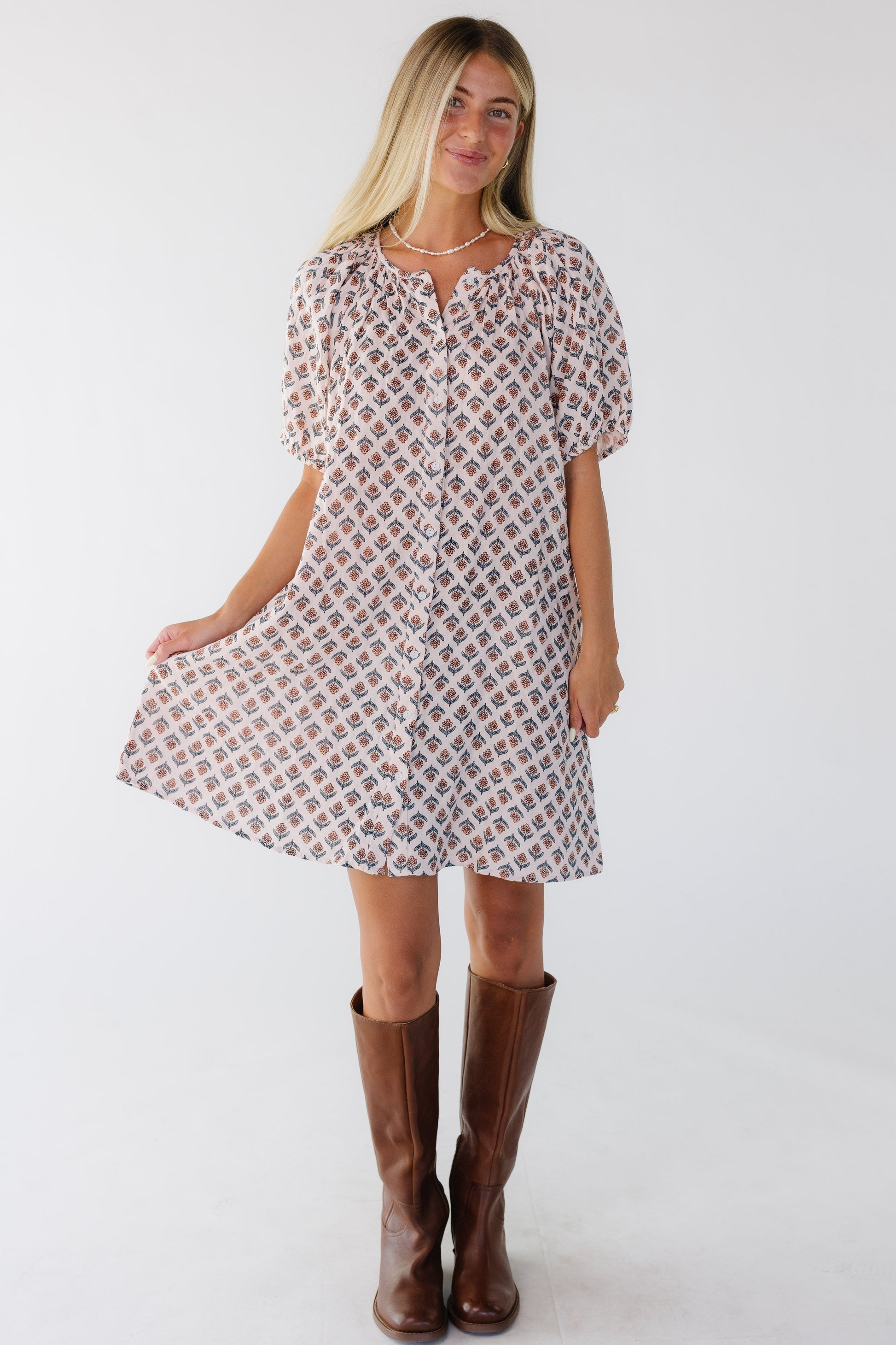 Woman wearing a pink floral short sleeve button down dress with a round neckline.