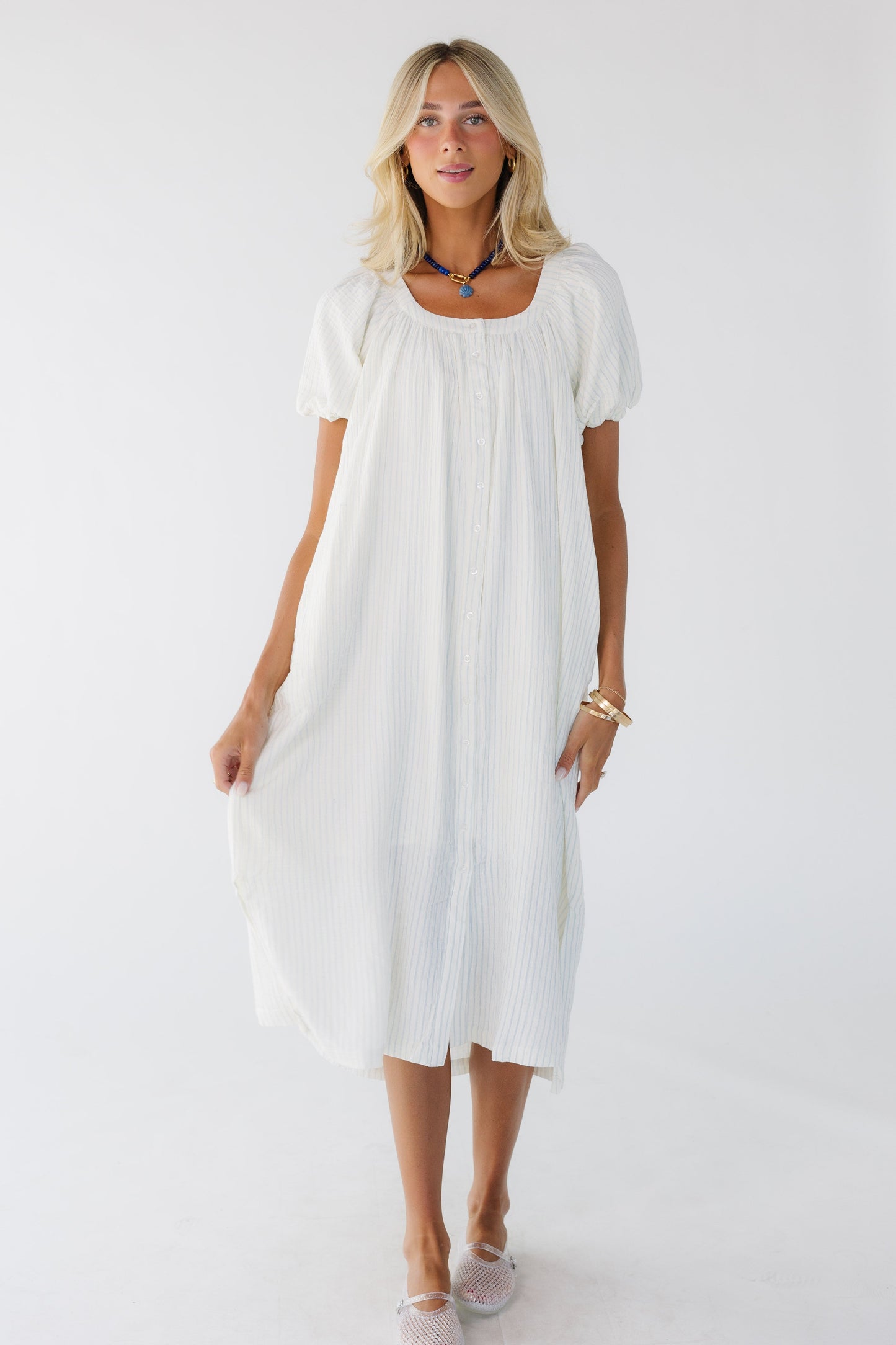 Young woman wearing a modest white & blue stripe button down midi-maxi dress with balloon sleeves and a scoop neckline.