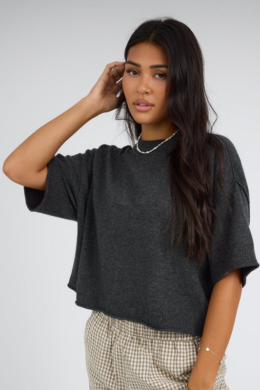 Young woman wearing a modest charcoal grey short sleeve sweater with a wide ribbed round neckline and rolled hems.