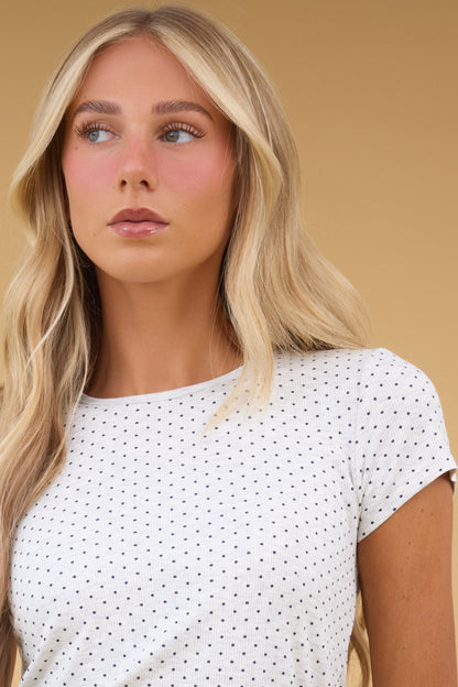 Woman wearing a greay and black dot knit to with short sleeves and a round neckline.