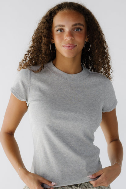 Young woman wearing a grey close fitting tee with shrot sleeves and a wide ribbed neckline.