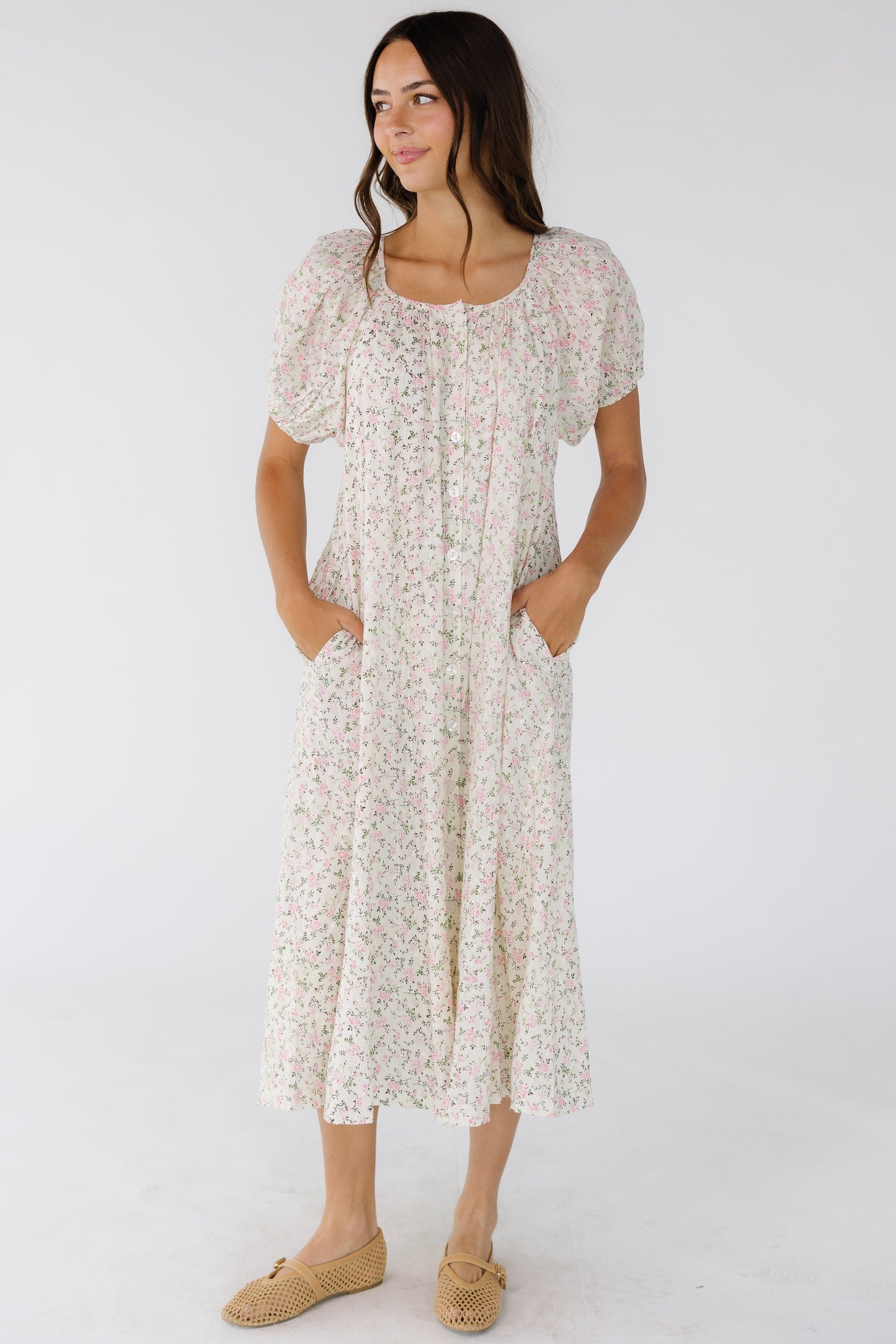 Young woman wearing a white button down dress with a scoop neckline, balloon  sleeves and side pockets. 