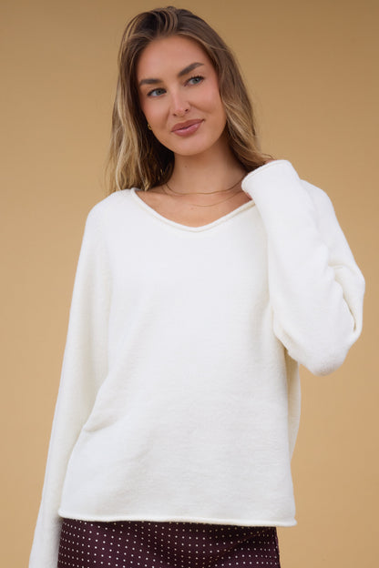 Young woman wearing a cream sweater wtih long sleeves, and a  wideV-neckline.