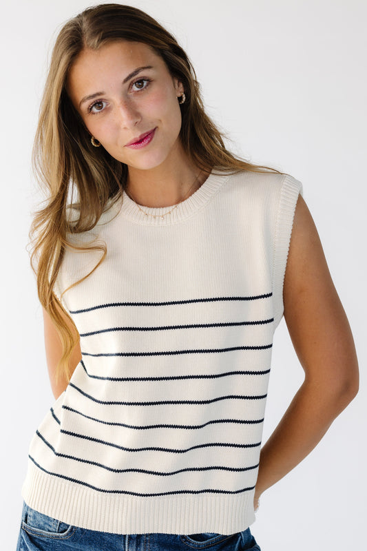 Woman wearing a natural pullover sweater vest with a crew neckline and thin black horizontal stripes that start part way down the vest.