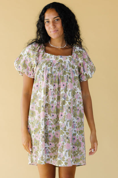 Young woman wearing a short floral dress in pink & green with balloon sleeves and a square neckline.