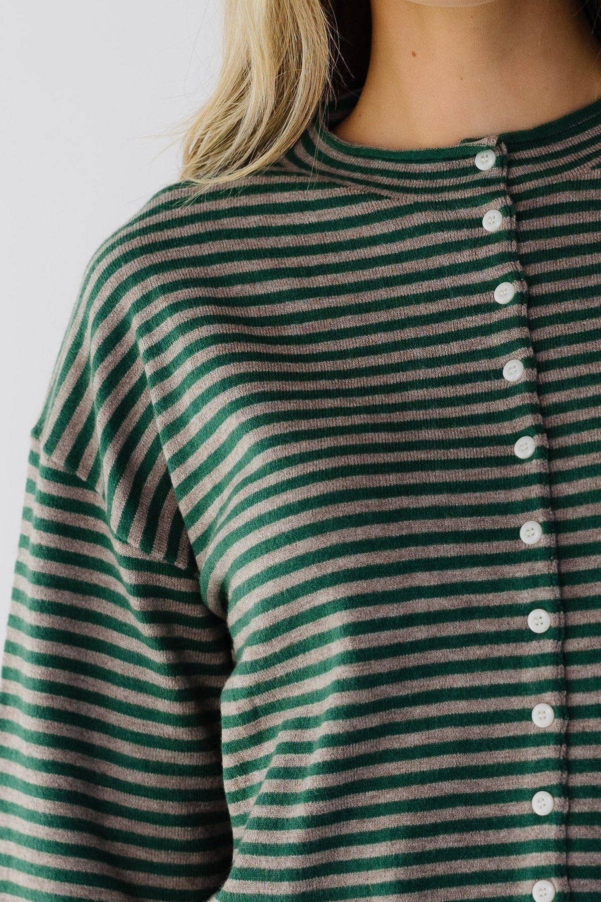 Close view of a woman wearing a taupe & green stripe button down cardigan.