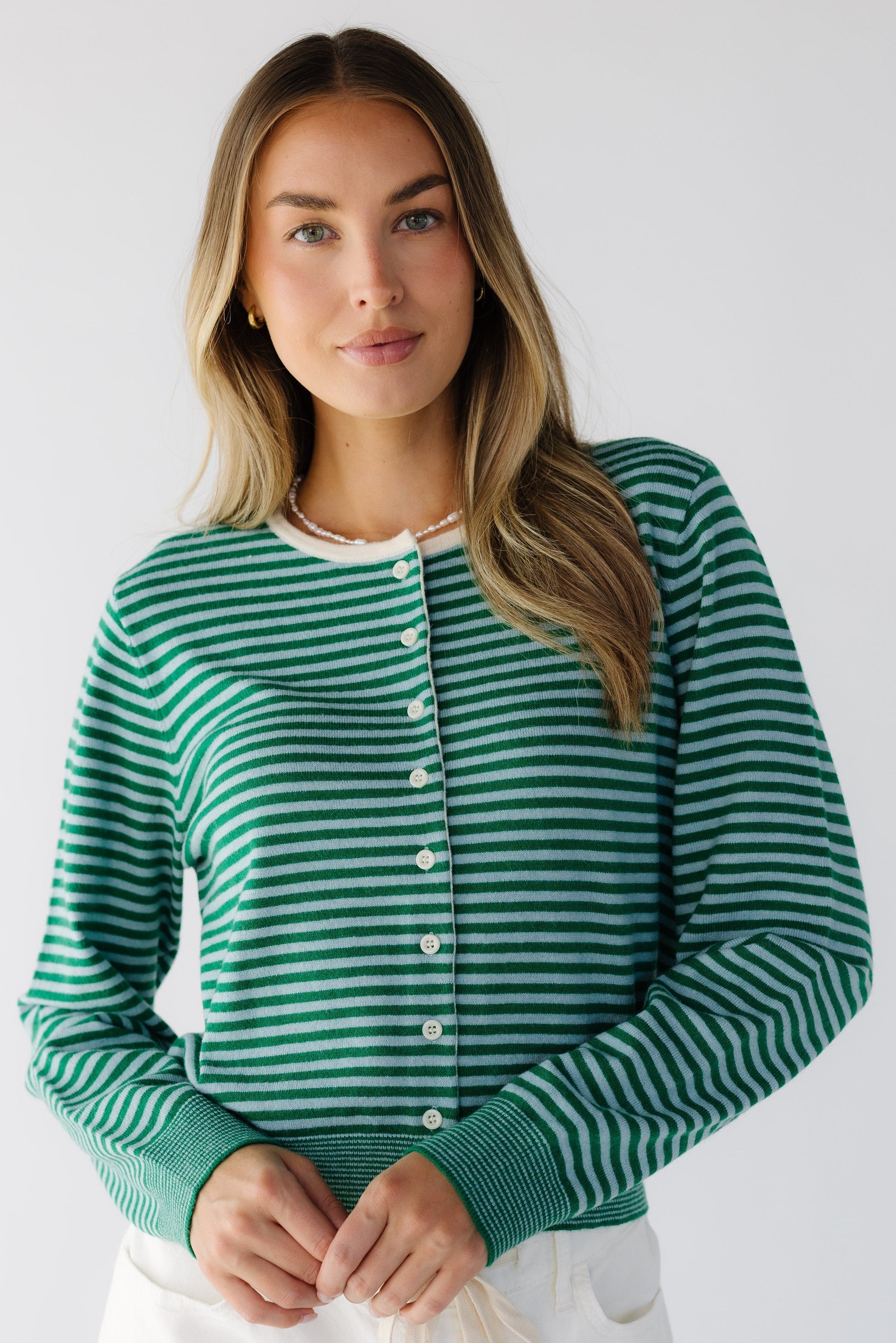 Young woman wearing a modest green & light blue stripe button down cardigan withcontrasting buttons and trimmed neckline. 