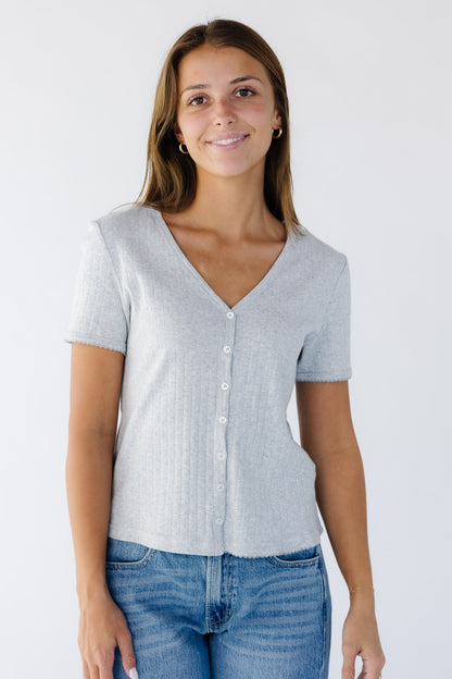 Woman wearing a  button down grey short sleeve top with a V-neckline. 
