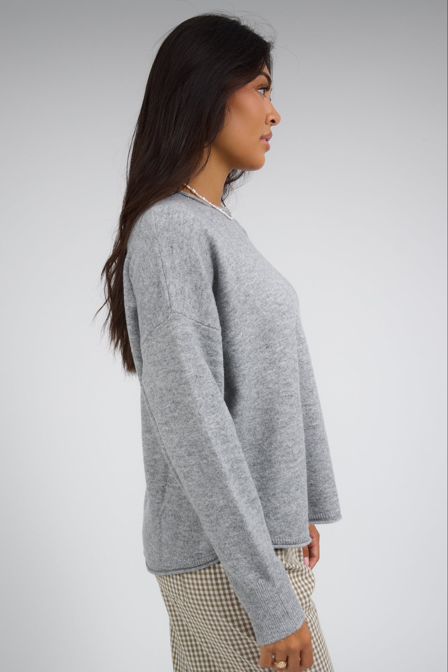 Side view of a woman wearing a heather grey pullover with drop shoulders and long sleeves.