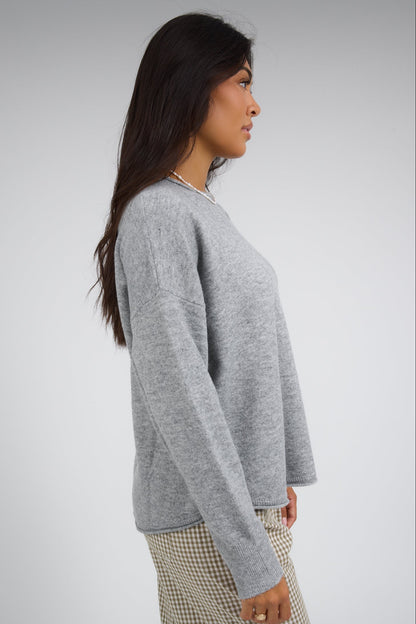 Side view of a woman wearing a heather grey pullover with drop shoulders and long sleeves.