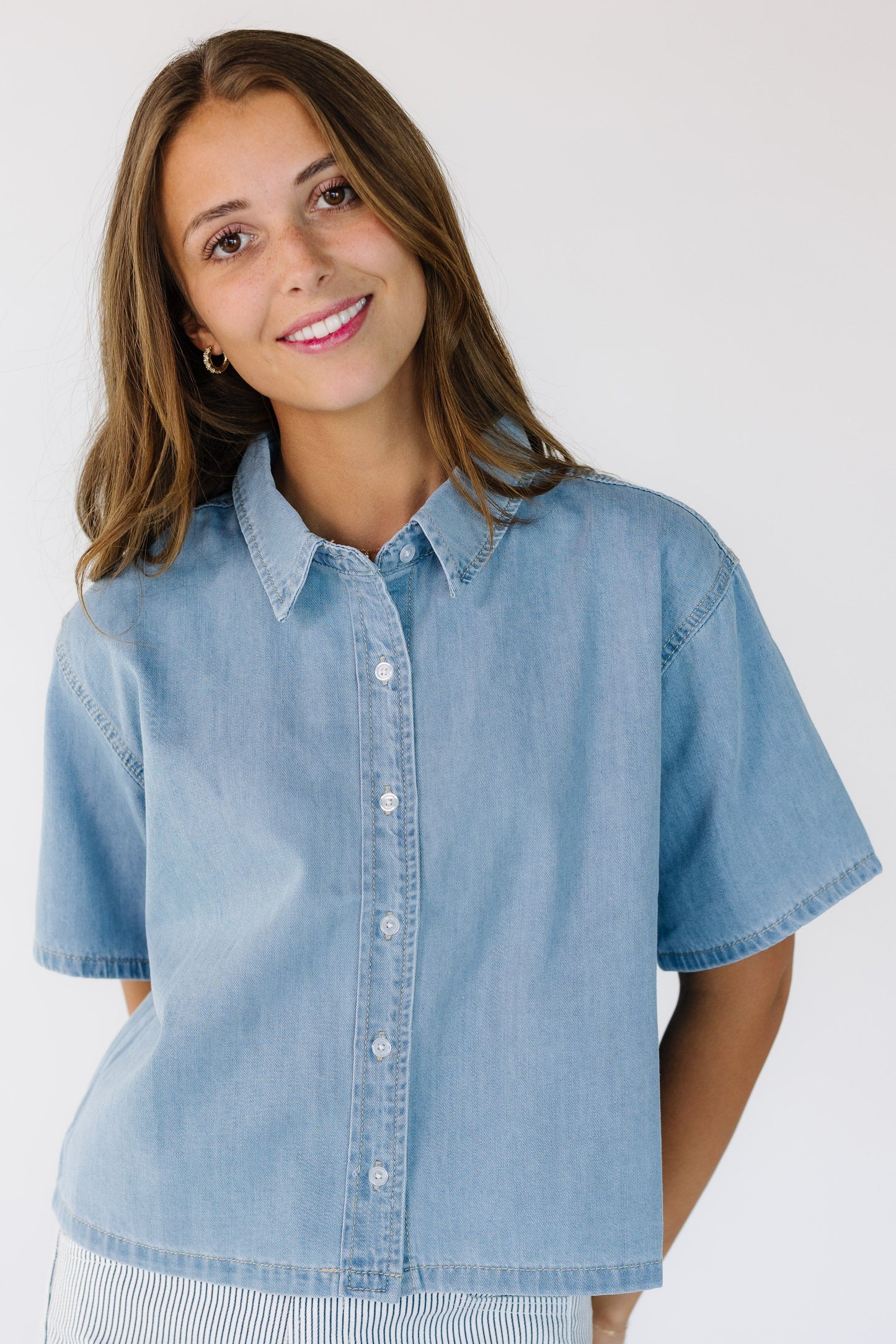 Young woman wearing a light denim button down top with short sleeves.