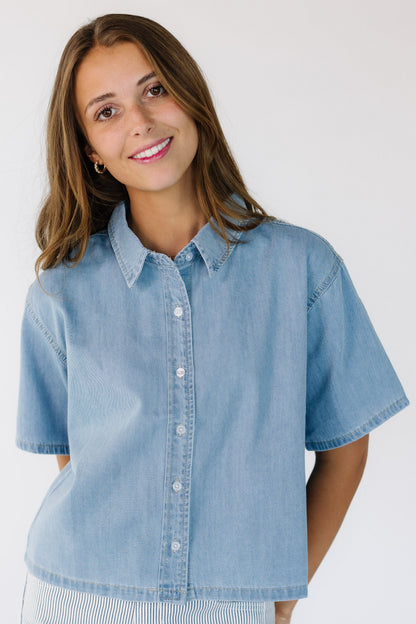 Young woman wearing a light denim button down top with short sleeves.