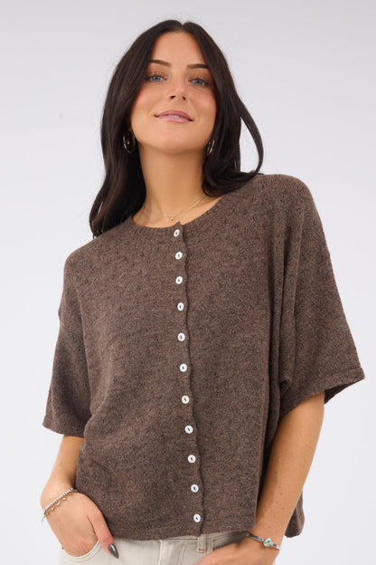A woman wearing a soft loose fitting button down cardigan in a brown pointelle knit.