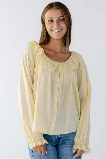 Woman wearing a light yellow flowy button down blouse with a wide lace trimmed ruffled collar and long sleeves with lace trimmed ruffle cuffs.