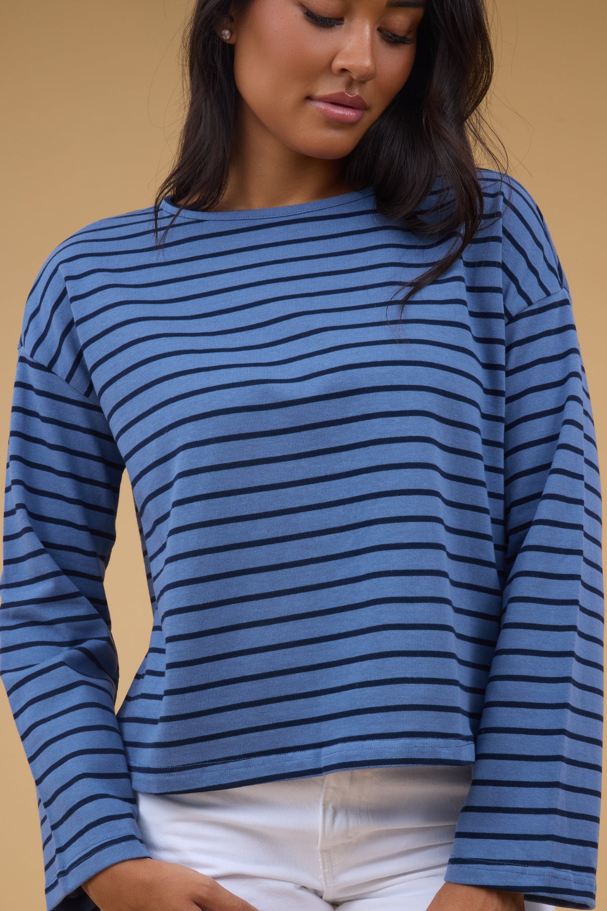 A young woman wearing a loose fitting blue & navy stripe long sleeve tee.
