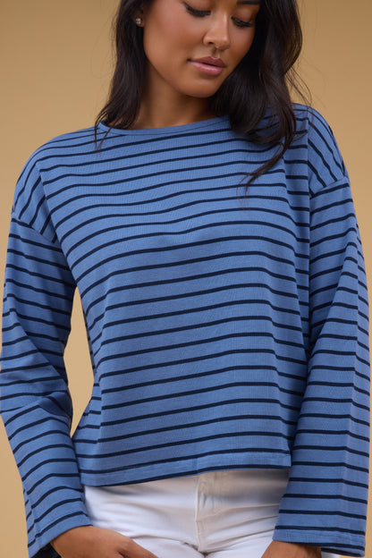 A young woman wearing a loose fitting blue & navy stripe long sleeve tee.