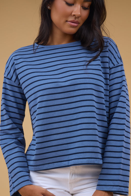 A young woman wearing a loose fitting blue & navy stripe long sleeve tee.