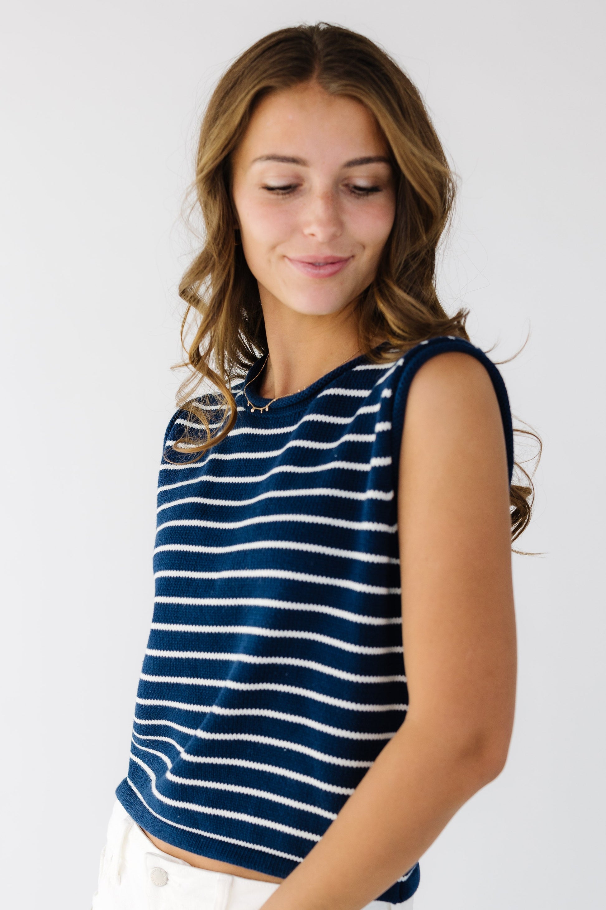 Woman wearing a navy sweater vest with white stripes and a round neckline.