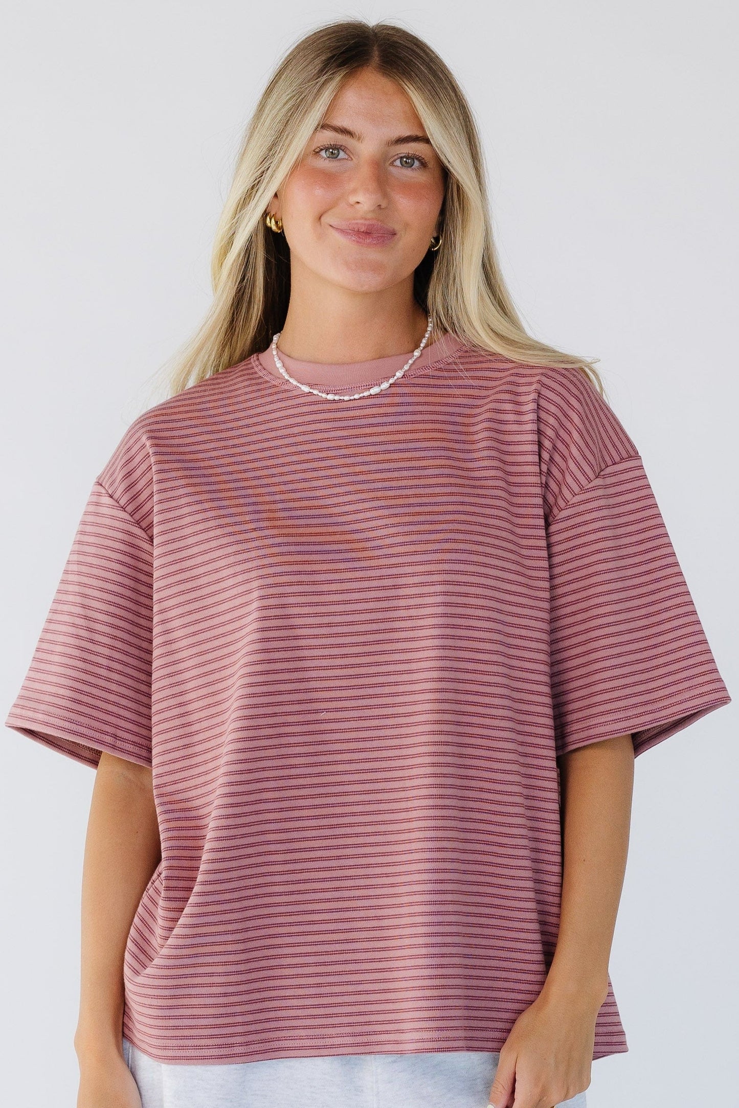 Young woman wearing a pink stripe loose fitting tee with short sleeves and a crew neckline.