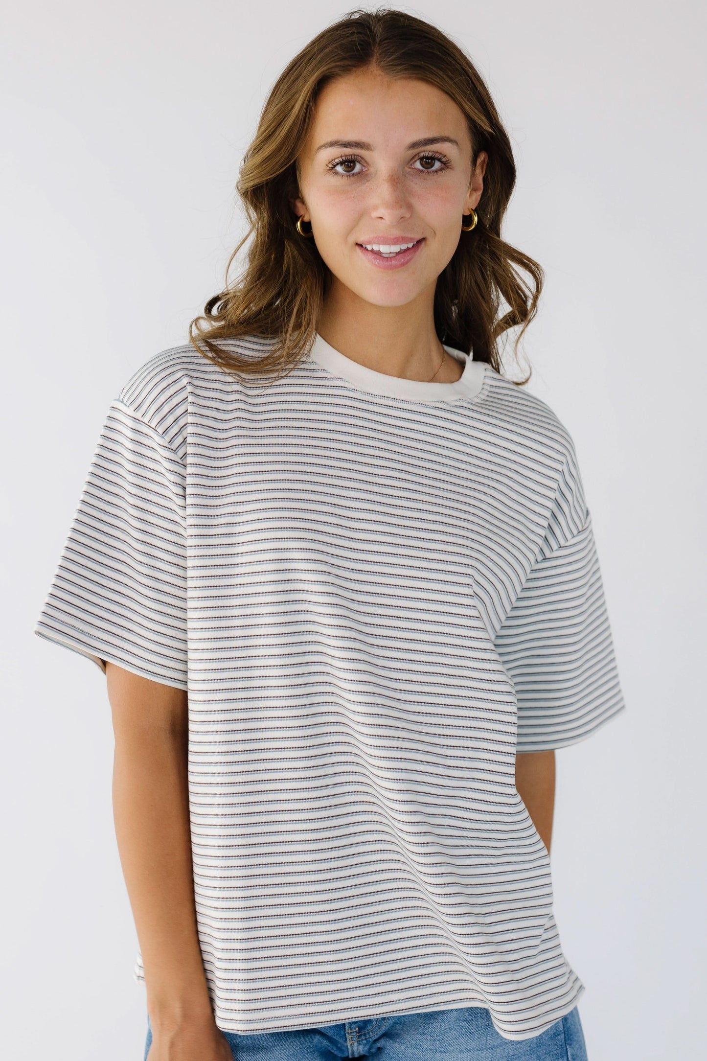 Young woman wearing a white stripe, loose fitting tee with short sleeves and a crew neckline. 