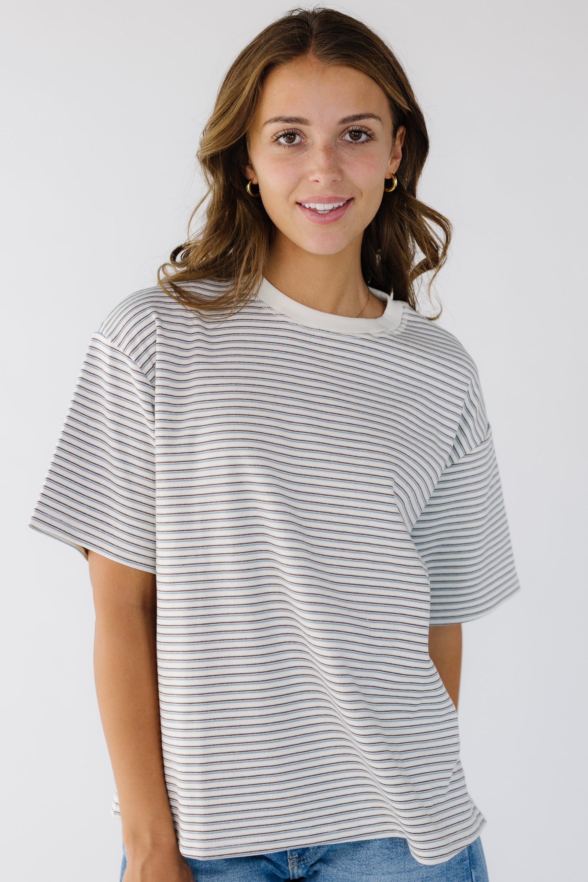Young woman wearing a white stripe, loose fitting tee with short sleeves and a crew neckline. 