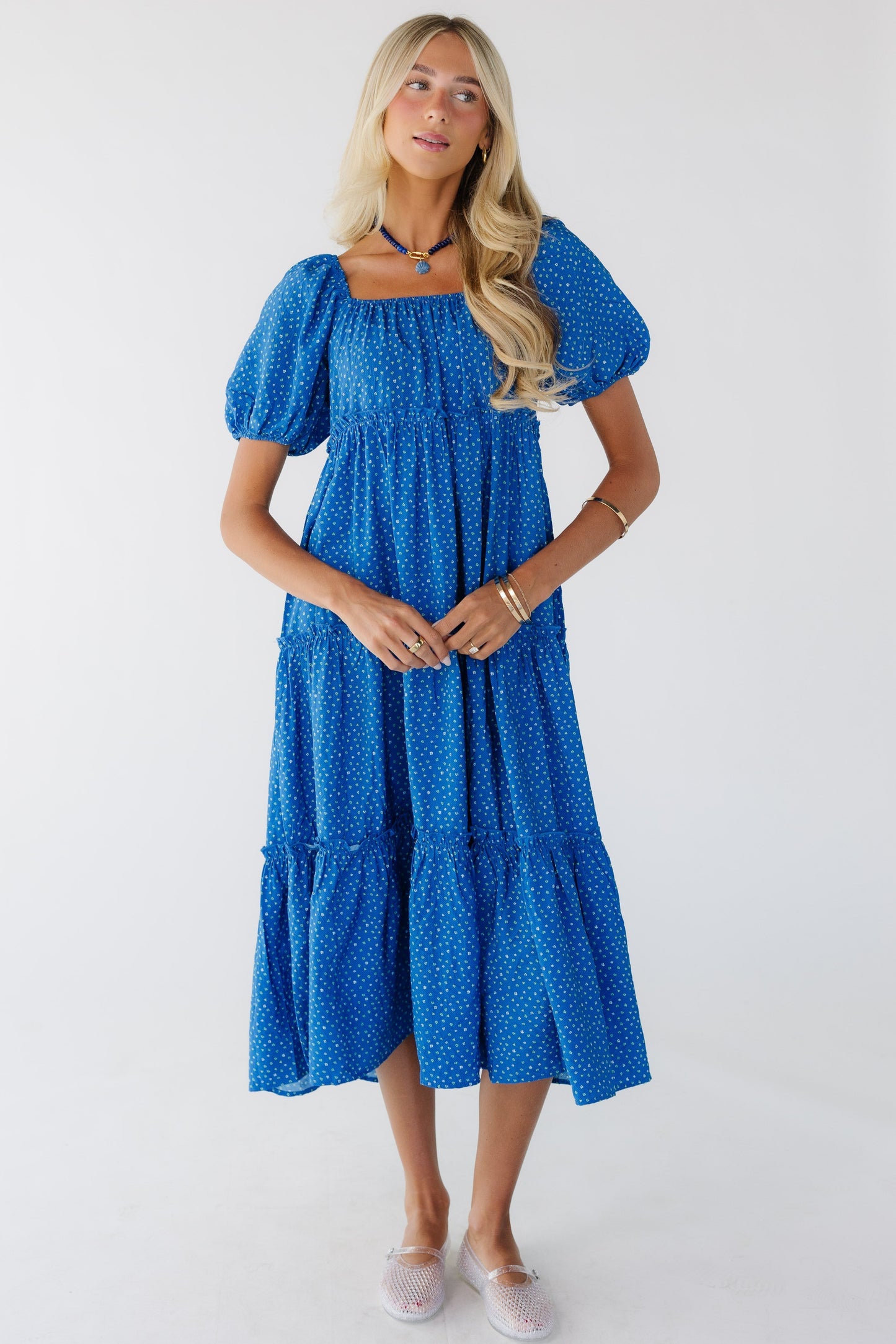 Woman wearing a loose fitting,  blue tiered midi dress with an elastic square neckline and balloon sleeves.