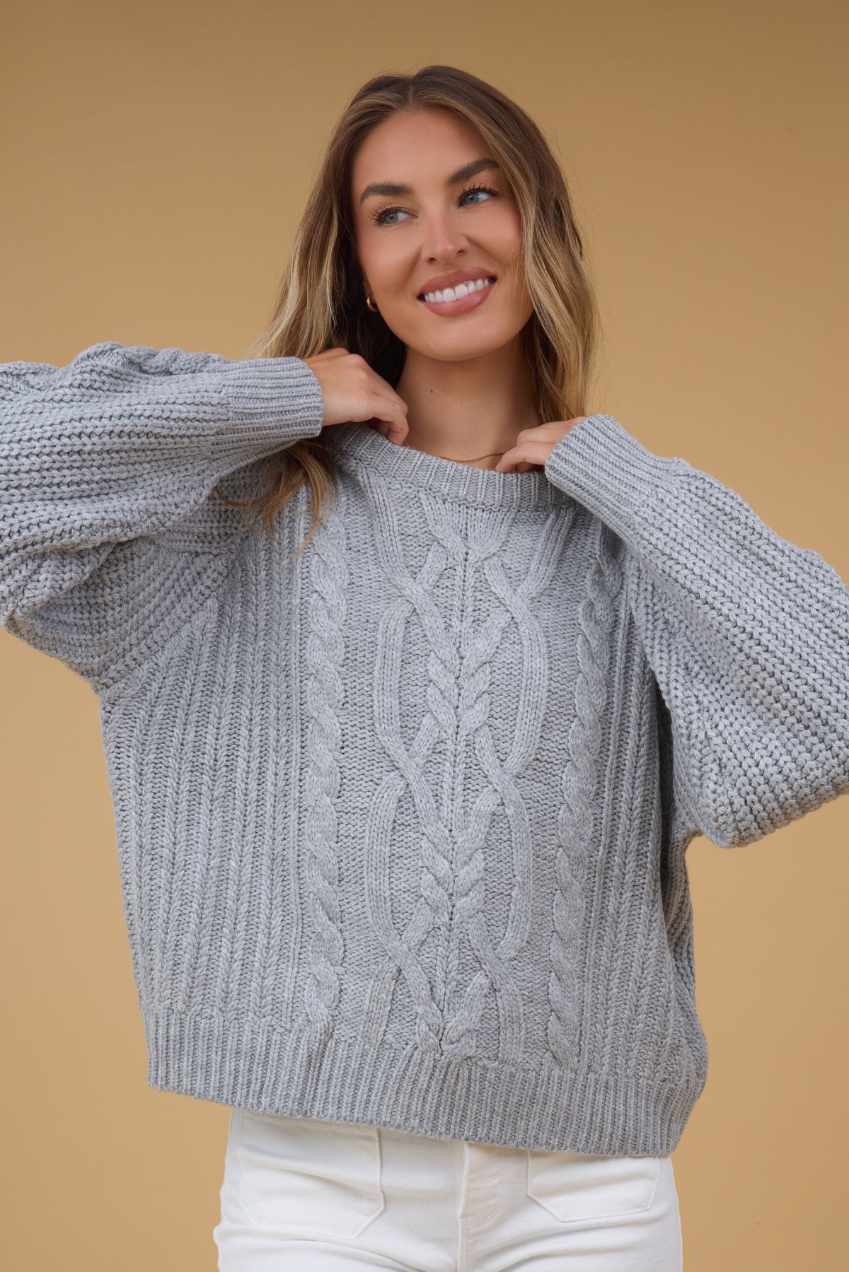Young woman wearing a modest loose fitting grey cable knit sweater.