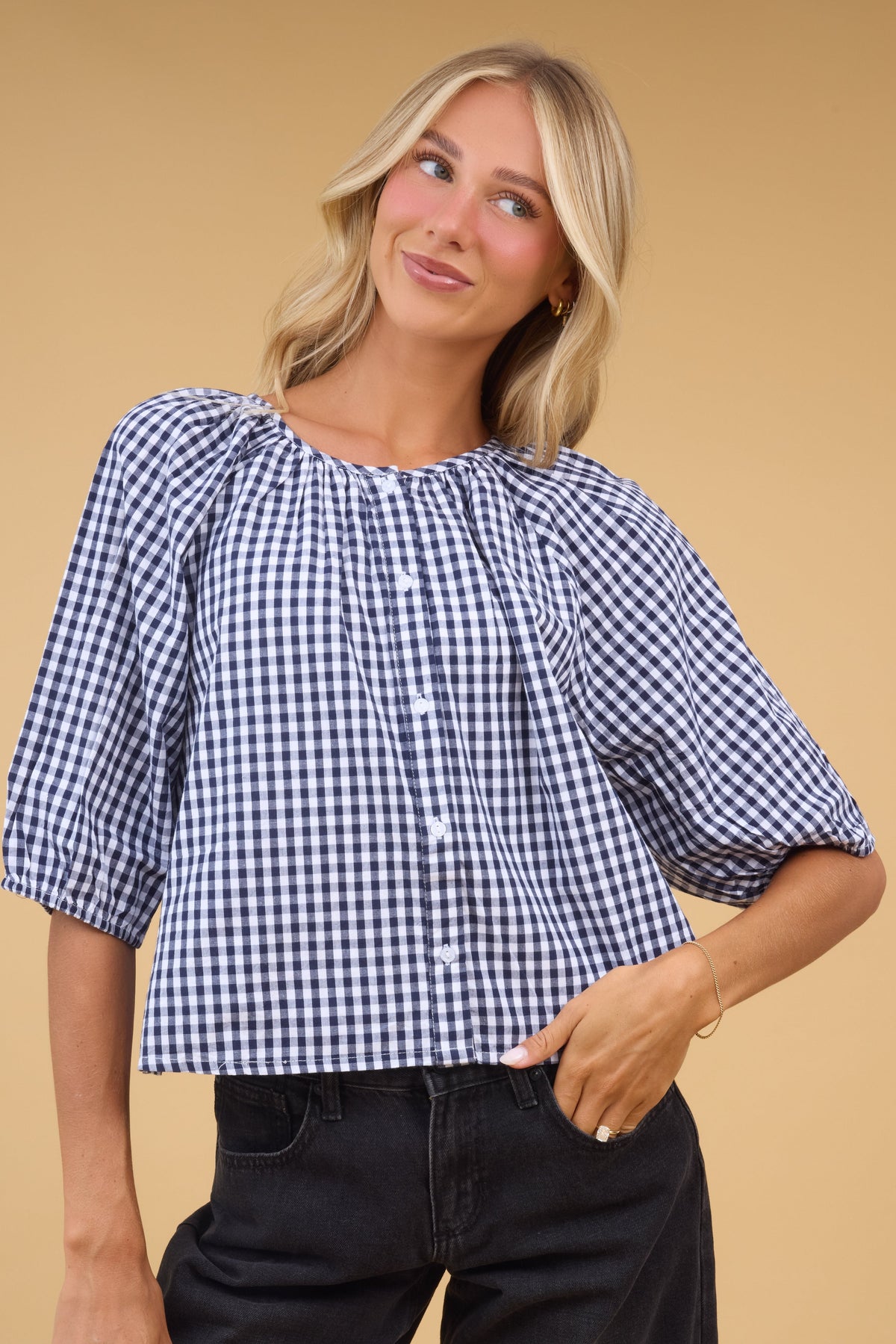 Young woman wearing a moest blue gingham button down top with a round neckline and half length sleeves.