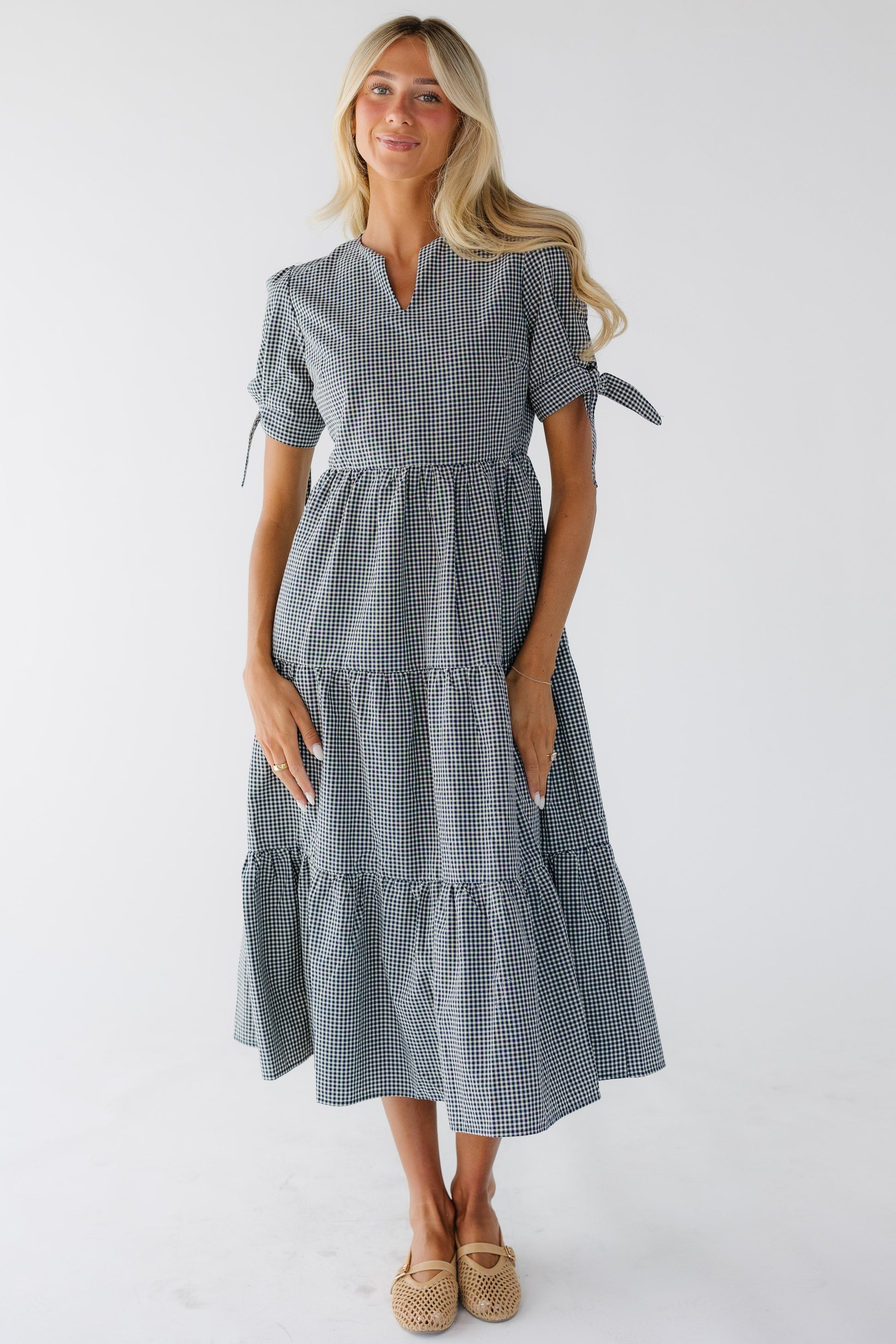 Young woman wearing a navy & white gingham tiered midi dess with a V-neckline and short tied sleeved