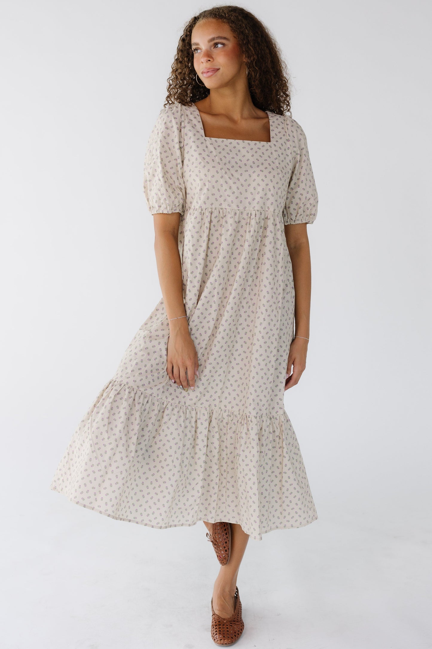 Woman wearing a cream print midi dress with a square neck line, puff sleeves and a wide bottom ruffle.