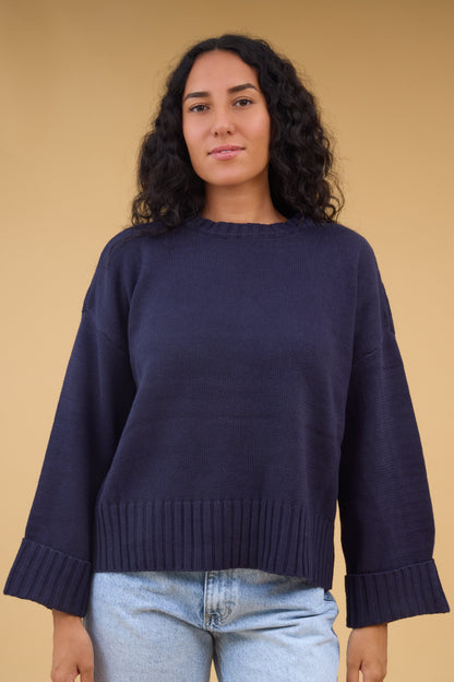 Woman wearing a loose fitting navy sweater with very wide ribbing at the cuffs and waist.