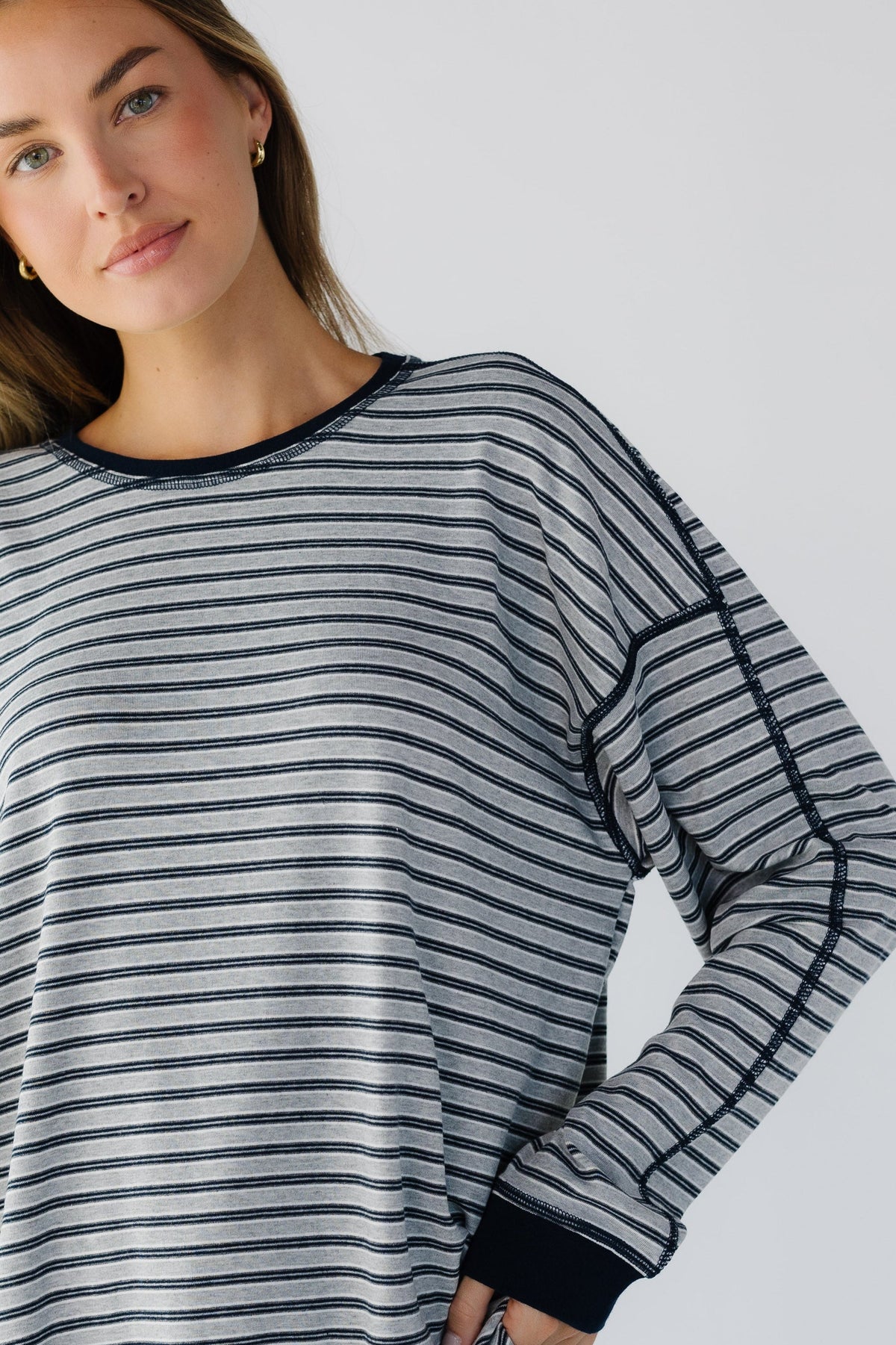 A close up view of a woman wearing an oversized long sleeve tee in a grey & navy stripe.
