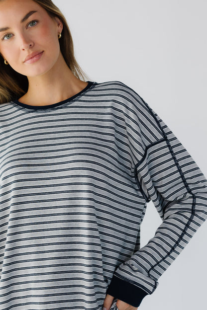 A close up view of a woman wearing an oversized long sleeve tee in a grey & navy stripe.