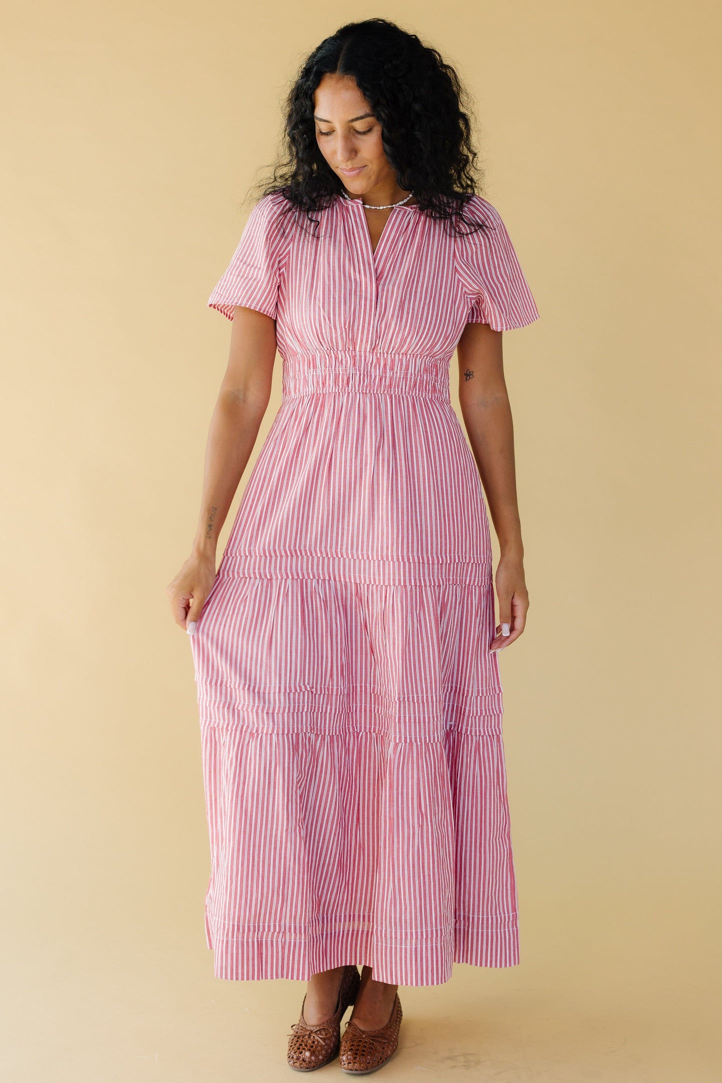 Woman wearing a red & white stripe midi-maxi dress with a full skirt with pleats and tiers, short sleeves and a wide elastic waist.
