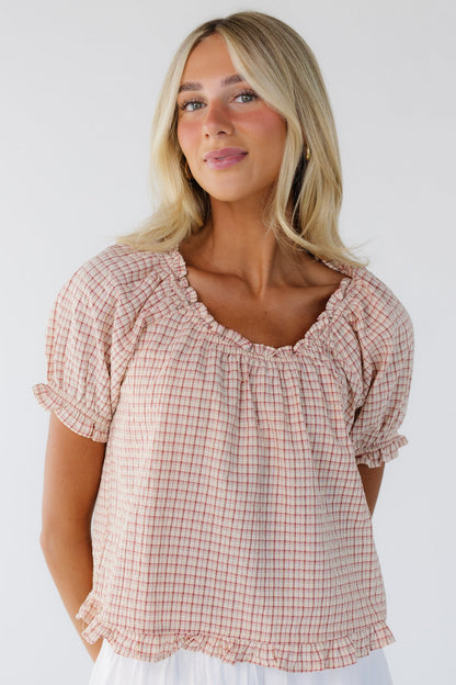 Young woman wearing a modest red plaid, loose fitting blouse with a ruffled scoop neckline, ruffled hem short puff sleeves, and a narrow ruffle bottom hem.