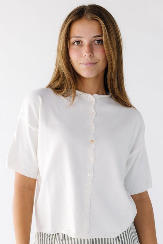 Woman wearing a modest white button down cardigan with short sleeves and a round rolled neckline.
