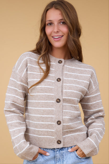 A woman wearing a taupe & white stripe cardigan with long sleeves and large buttons.