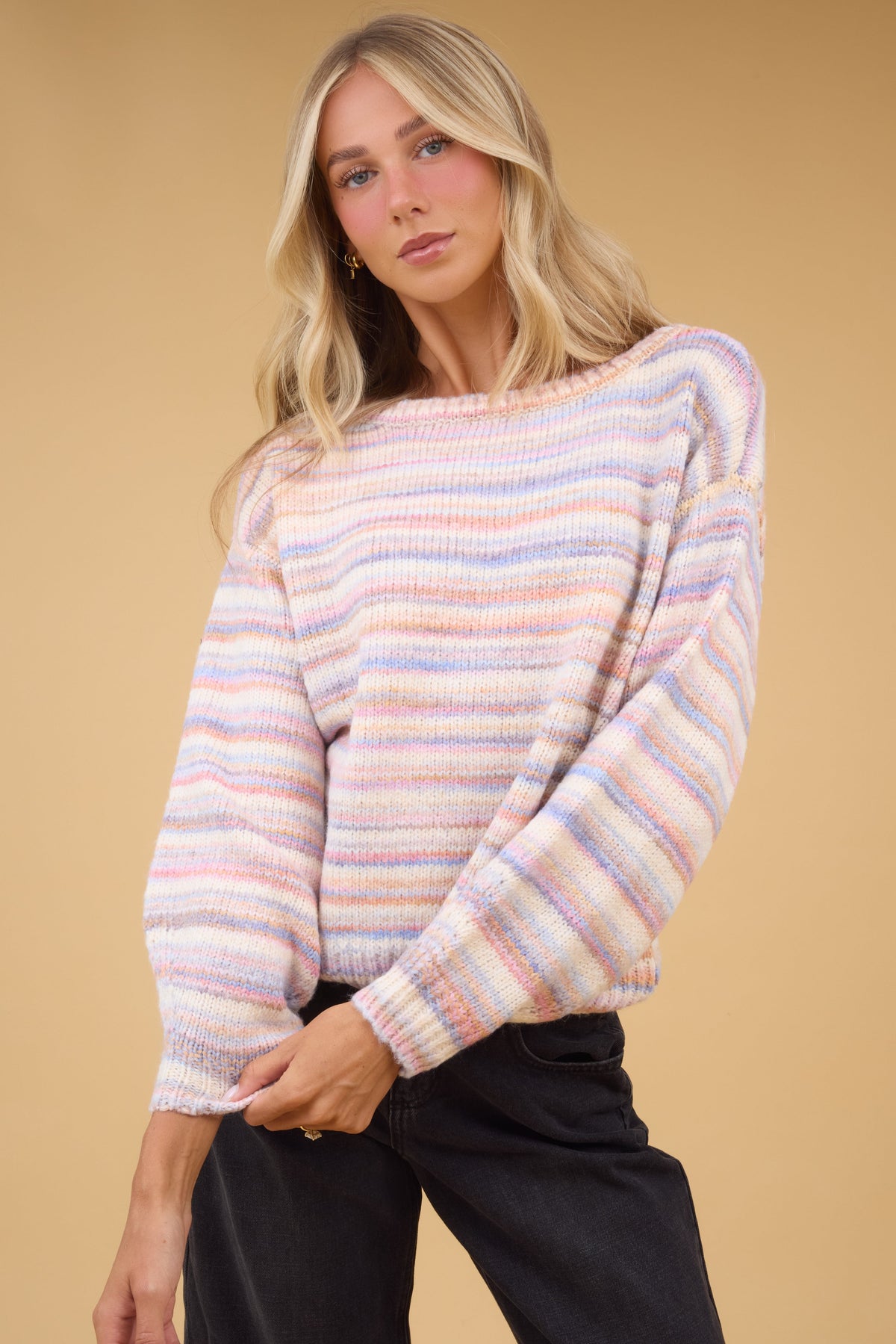 Young woman wearing a loose fitting softly colored rainbow stripe pullover with long sleeves.