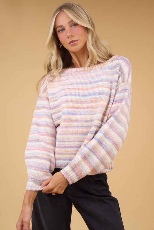 Young woman wearing a loose fitting softly colored rainbow stripe pullover with long sleeves.