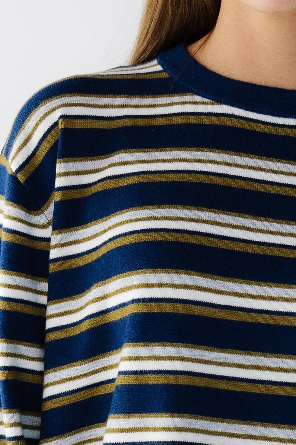Close view of a woman wearing a navy, white, tan & grey stripes with a crew neckline and long sleeves.