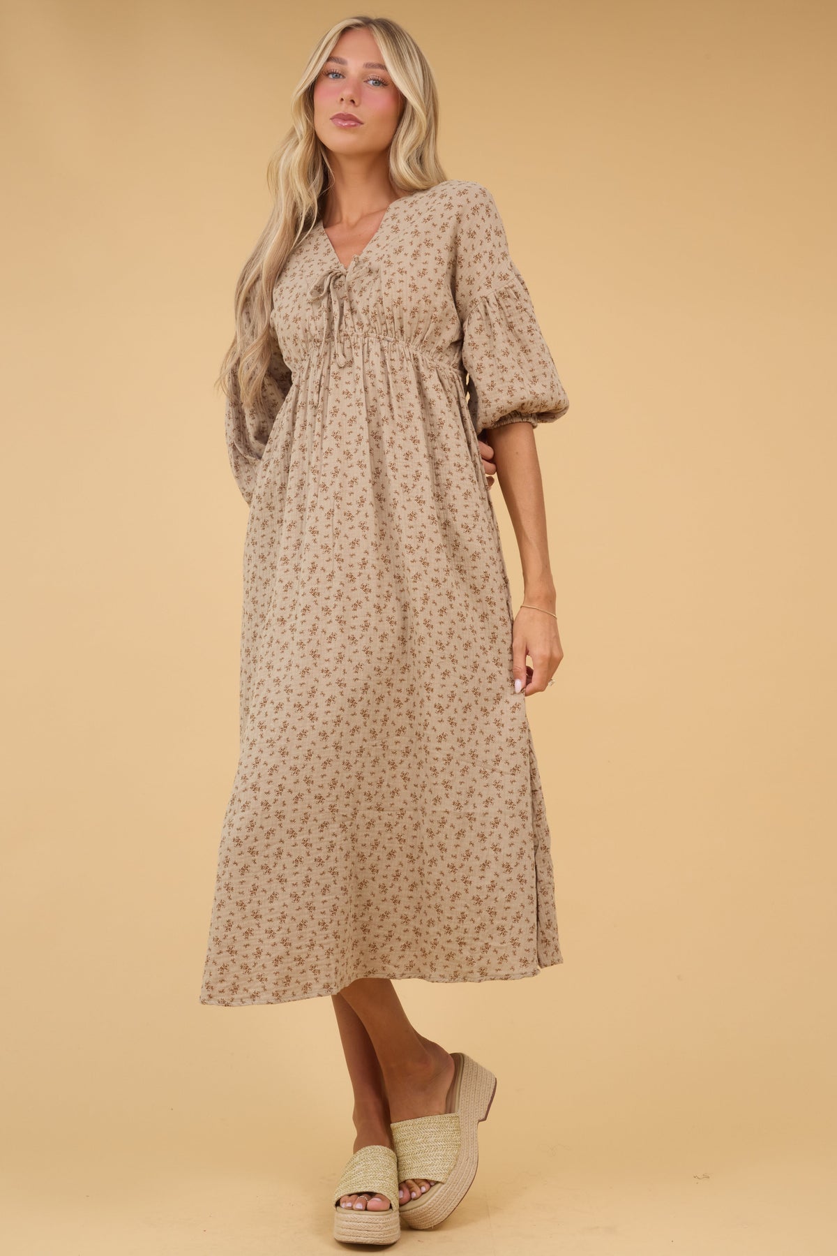 Woman wearing a floral midi dress in tan with an elastic empire waist, half length sleeves and a V-neckline.