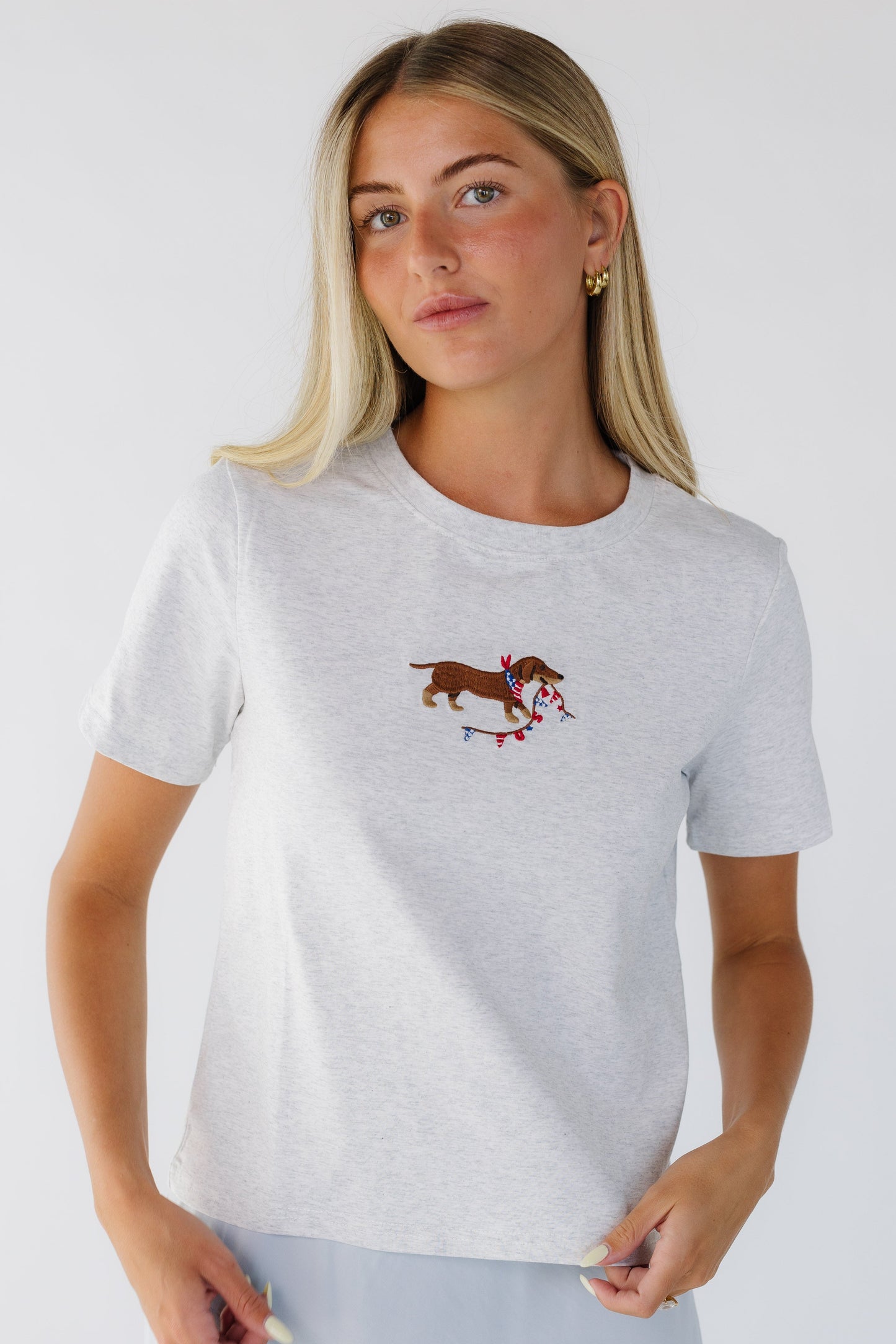 Young woman wearing a heather grey tee with an embroidered dog & USA banner and short sleeves.