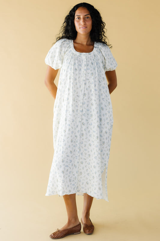 Young woman wearing a modest white & blue floral print midi dress that buttons down the front with balloon sleeves and a scoop neckline.