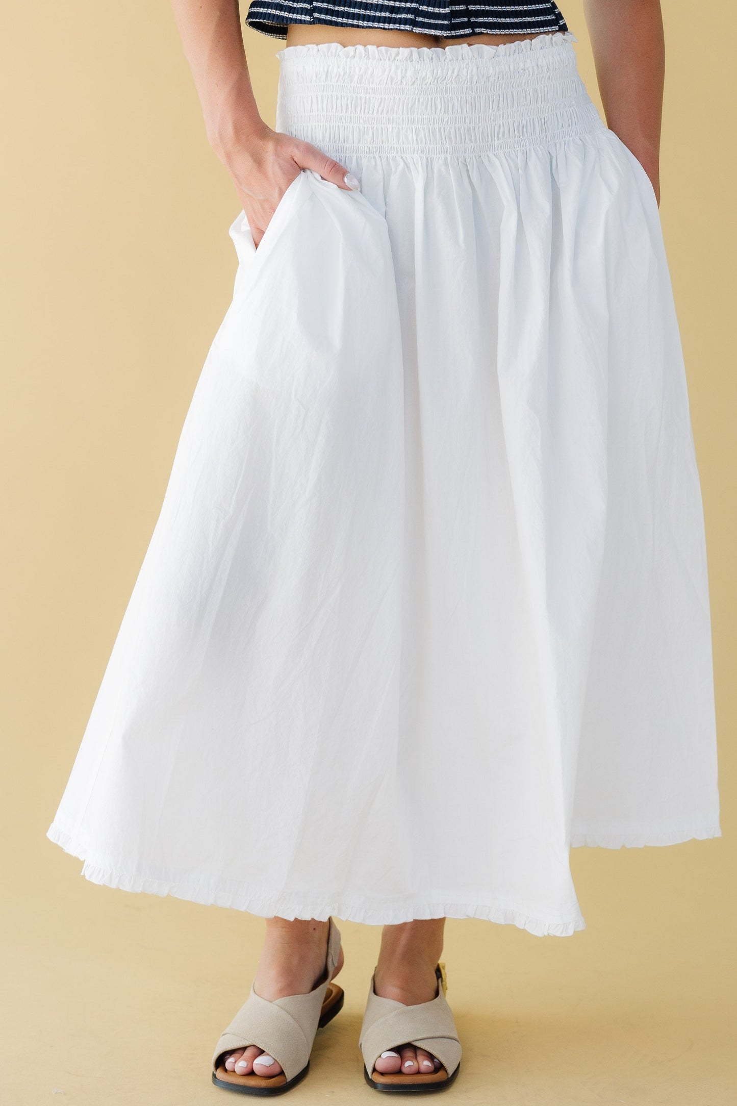 Woman wearing a very full gathered skirt with side pockets and a wide elastic smocked waist and a narrow ruffle hem.