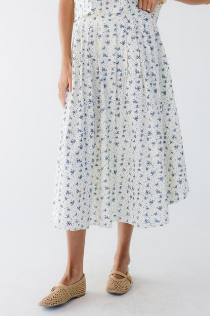 Woman wearing a cream & blue print, pleated midi skirt.