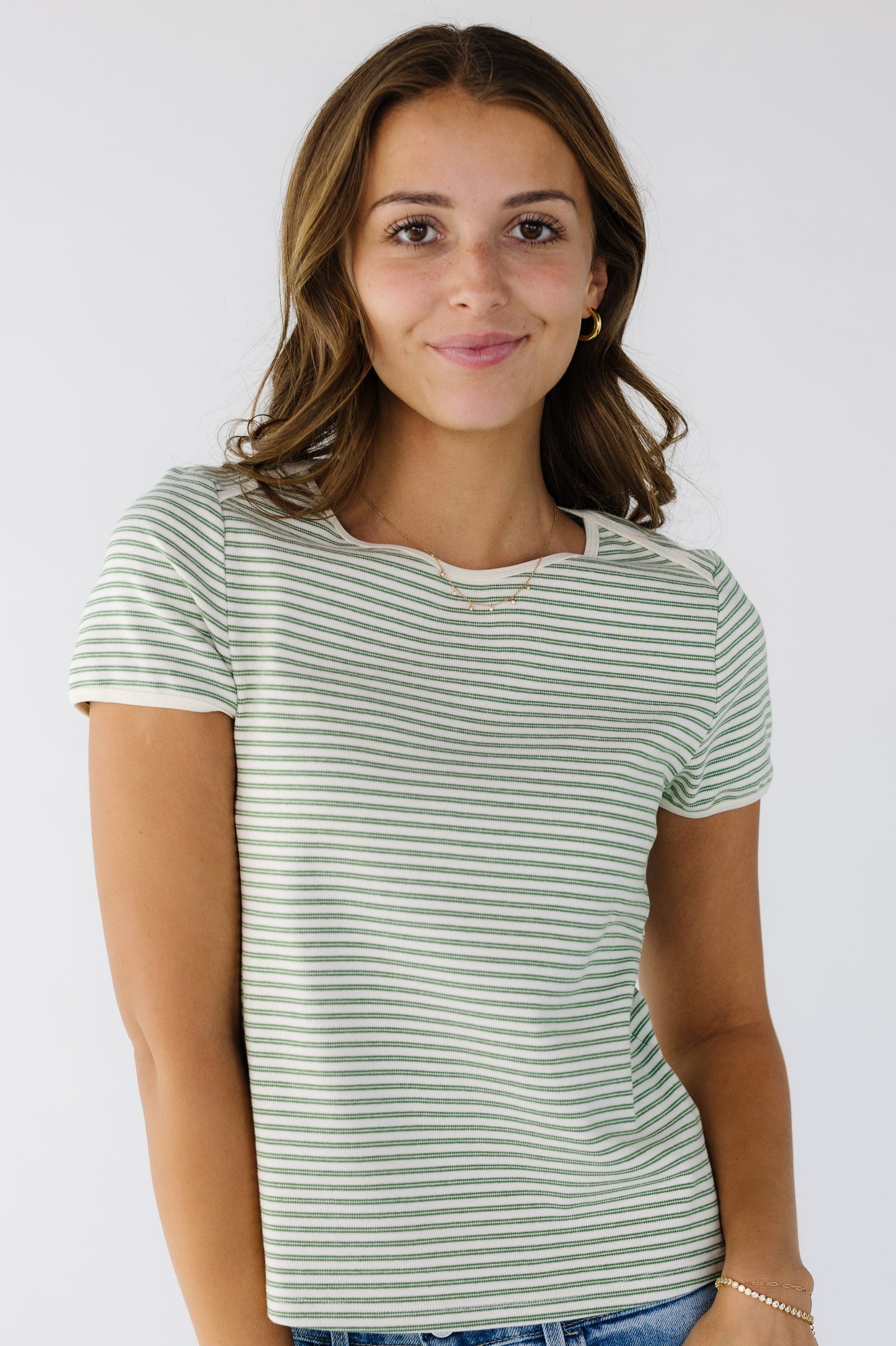 Young woman wearing an closer fitting knit top in ivory and double green stripes with short sleeves and a round trimmed neckline. 