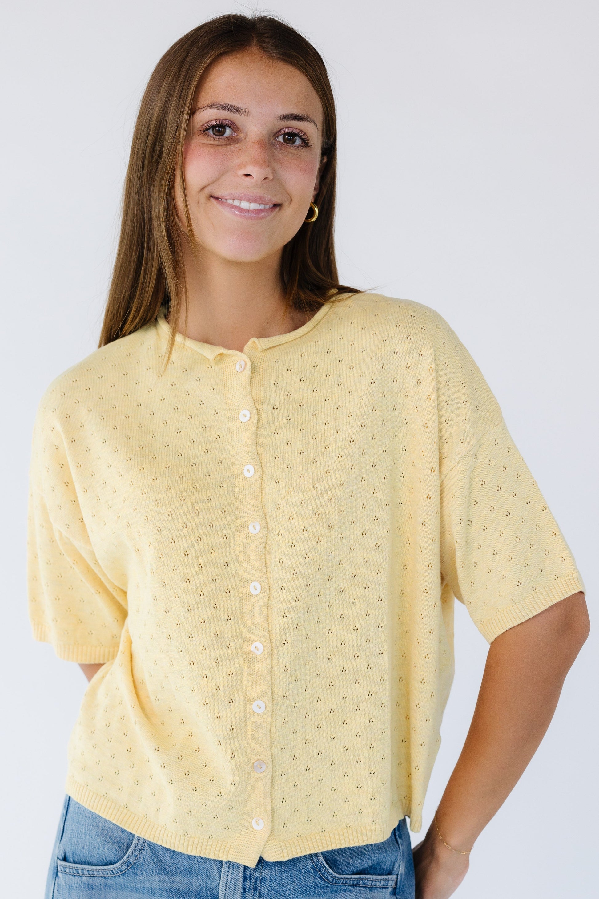 Woman wearing a light yellow pointelle eyelet knit, button down cardigan with short sleeves and a rolled collar.