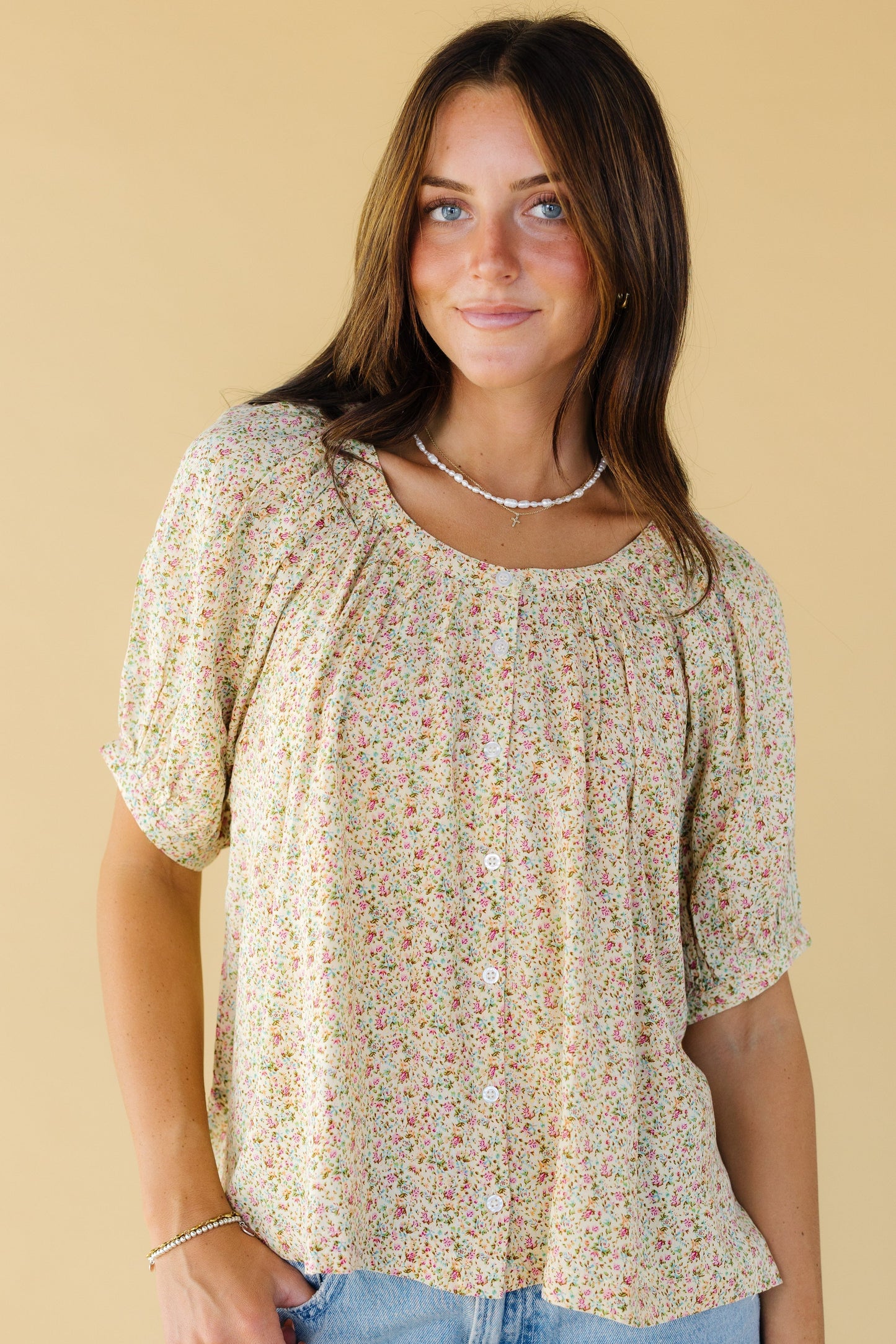 Young woman wearing a modest yellow floral button down blouse with short puff sleeves an a round neckline.