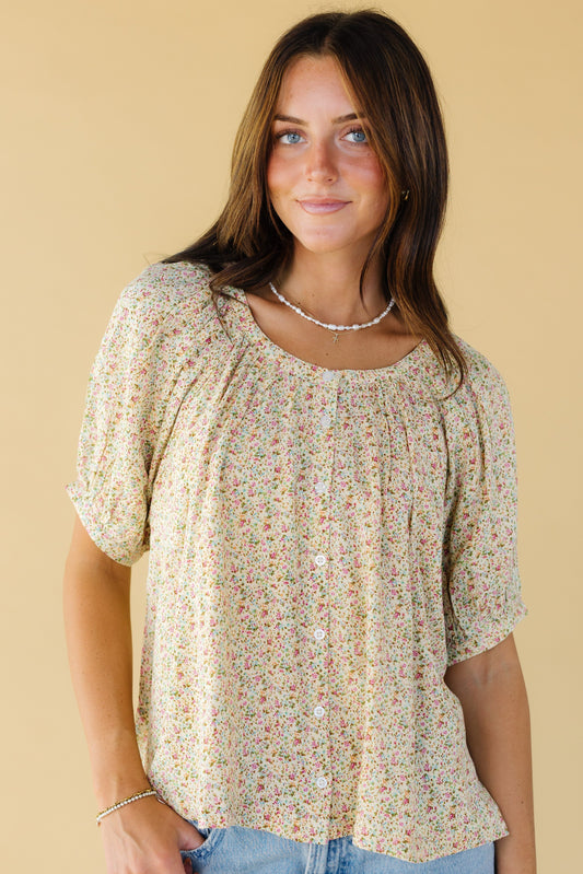 Young woman wearing a modest yellow floral button down blouse with short puff sleeves an a round neckline.